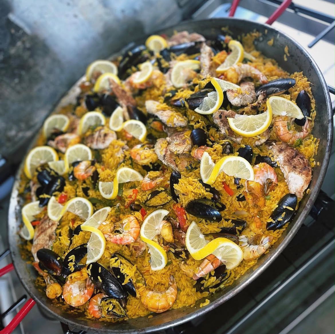 Large paella pan with saffron rice, shrimp, mussels and lemon wedges